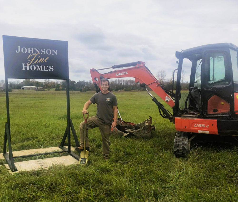 Andrew Johnson holding a shovel standing in front of a Johnson Fine Homes sign.